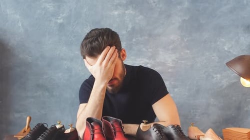 Man Contemplating Shoes at Desk Indoors