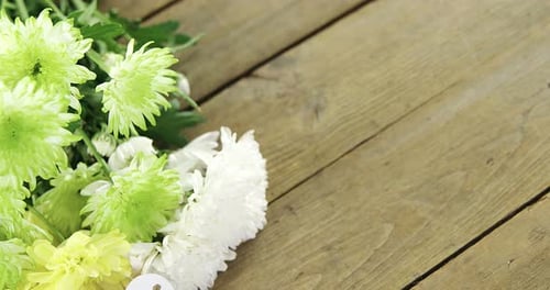 Bunch of yellow flowers with heart shape tag on wooden plank
