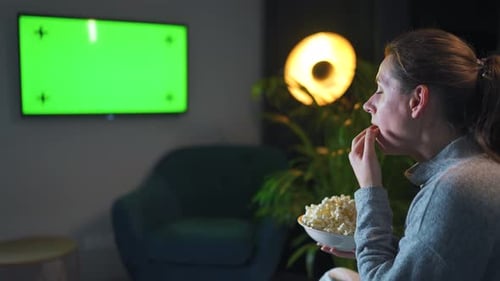 Woman Sitting on a Sofa in the Living Room in the Evening and Watching a Green TV Screen Mockup