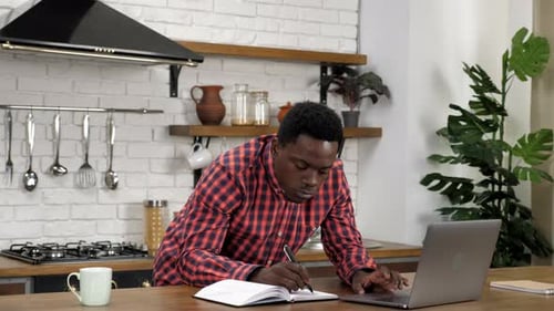 Young Adult Works at Laptop in Modern Kitchen