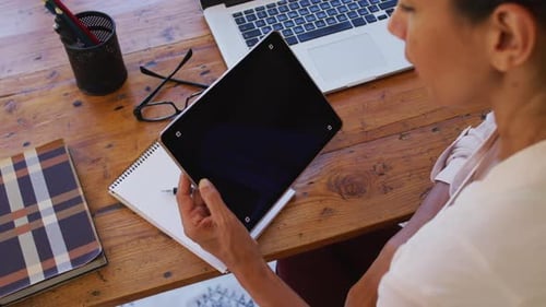 Woman Holds Tablet at Wooden Desk