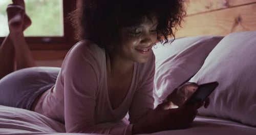 Mixed race woman using smartphone in bedroom