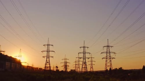 High-voltage electric line at sunset. Silhouettes of electric pylons on the setting sun background.