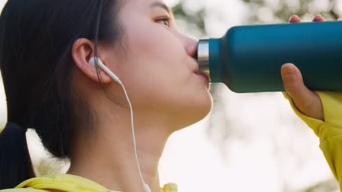 Asian sportswoman drinking from water bottle after running at the street in urban.