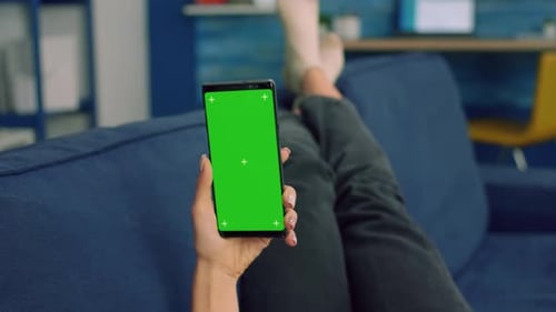 Freelancer Woman Lying on Sofa Looking at Mock Up Green Screen Chroma Key Smartphone