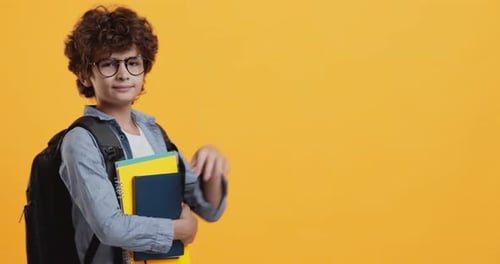 Boy With Books Waving Against a Yellow Background