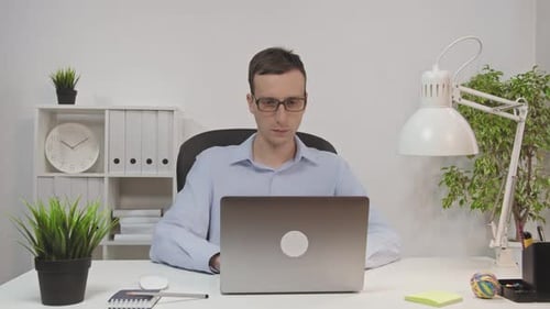 Young Businessman in Glasses Working with Laptop Computer in Modern Office Typing Looking at Screen