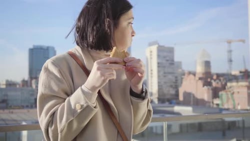 Woman Eats Sandwich with a City View