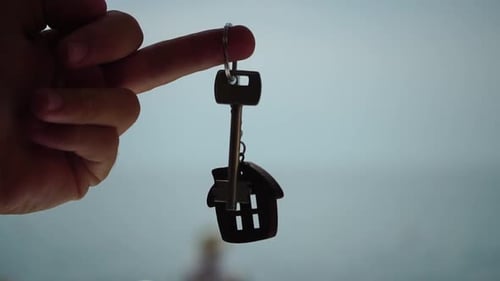 Llaves con un llavero en forma de casa en la mano de un hombre sobre fondo de playa marina