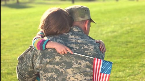Loving Child Hugging Soldier in Field with Flag