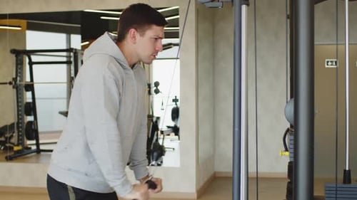 Joven con capucha gris entrenando brazos en un gimnasio