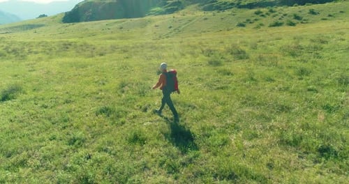 Flight Over Backpack Hiking Tourist Walking Across Green Mountain Field. Huge Rural Valley at Summer