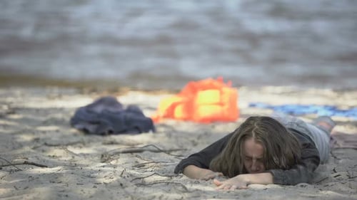 Mulher miserável deitada na praia, sentindo-se mal, sobrevivente de refugiado de naufrágio