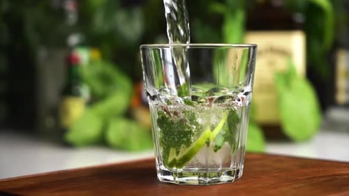 Mojito Being Poured into Glass With Lime and Mint