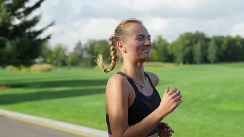 Smiling Sportswoman Jogging in Green Park. Woman Doing Morning Workout