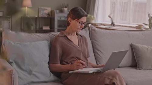 Woman Working on Laptop and Writing in Notebook