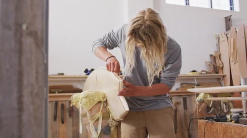 A Caucasian male surfboard maker polishing a wooden surfboard edge