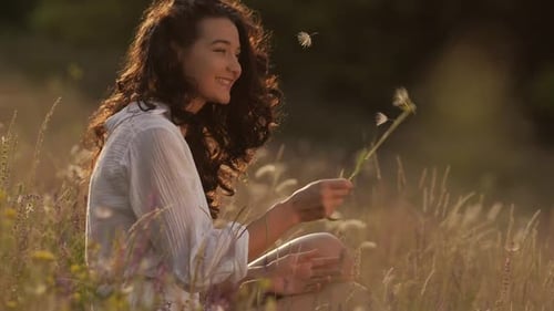 Woman Enjoys a Dandelion in Meadow at Sunset