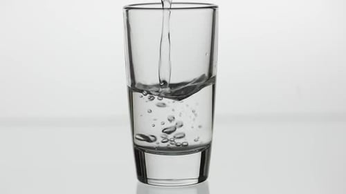 Pouring Up Shot of Vodka Into Drinking Glass. Slow Motion. White Background