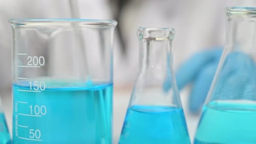 Lab scientist pouring liquid in lab flask. Close up of female scientist doing laboratory experiment