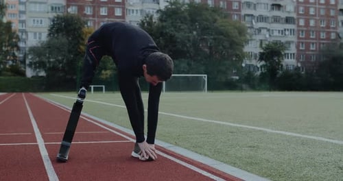 Disabled Guy with Prosthetic Running Blades Stretching While Standing at Sports Field