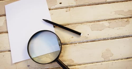 Magnifying glass, pen and paper on wooden plank