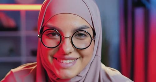Arabische Frau im Kopftuch, die Brille trägt und mit zufriedenem Gesicht vor der Kamera posiert