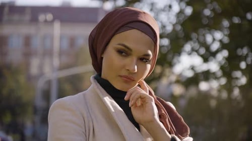 A Young Beautiful Muslim Woman Thinks About Something and Nods in a Park in an Urban Area Closeup