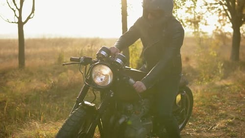 Young Man in Helmet and Leather Jacket Comes Up to His Bike and Starts the Engine While Standing on