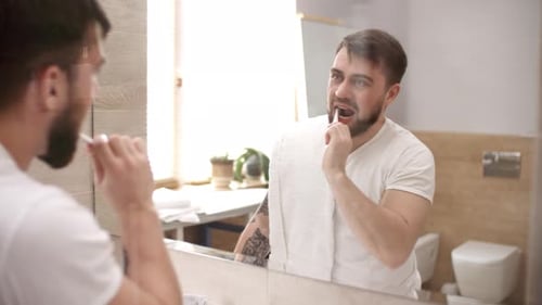 Handsome Caucasian Man Brushing Teeth in front of Mirror