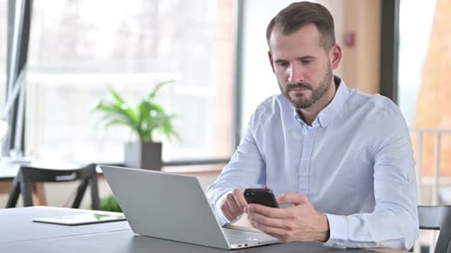 Young Man Using Laptop and Smartphone in Office