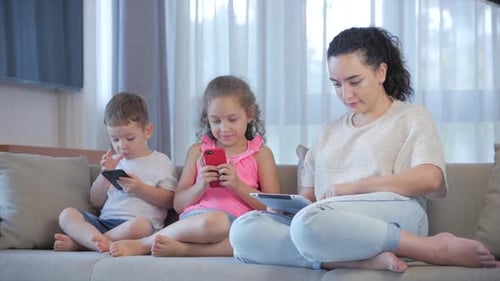 Family Using Phones and Tablet on Couch Indoors