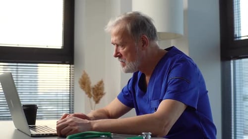 Seitenansicht eines professionellen reifen männlichen Arztes in blauer Uniform mit Laptop im Büro