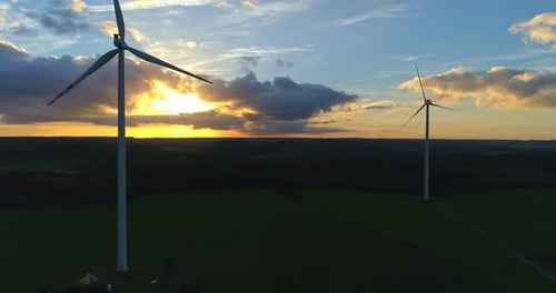 Wind Turbines Turning at Sunset Over Green Fields
