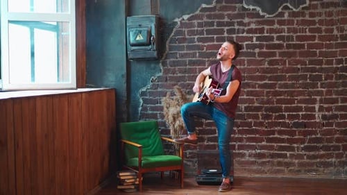 Young Man Singing and Playing Guitar Indoors