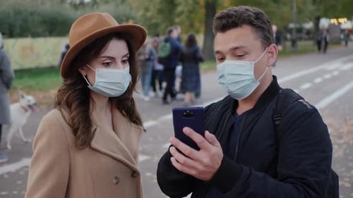 Couple with Face Masks Looking at Smartphone in Park