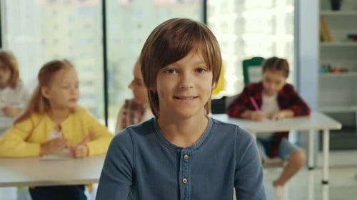 Smiling Boy in Classroom with Students Writing