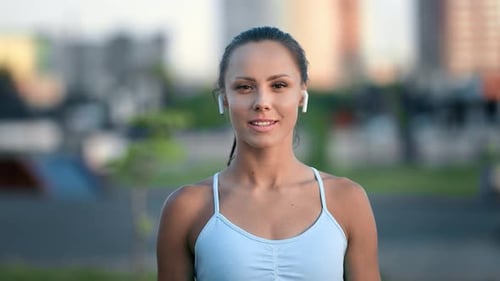 Portrait of Smiling Fitness Woman in Earphones Posing Outdoor City Street Sports Ground Cityscape