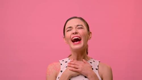 Mulher ri em voz alta do homem à sua frente no fundo de uma parede rosa.