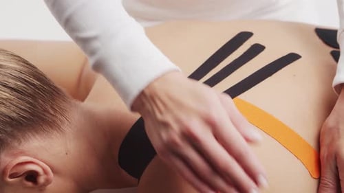 Applying Therapeutic Tape to Woman's Back for Pain