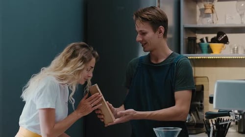 Barista in a coffee shop putting beans in a craft bag and sells it for female customer