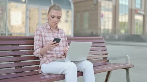 Young Woman Using Smartphone and Laptop While Sitting Outdoor on Bench