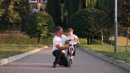 Dad Teaching Son To Drive a Bike in the Summer Park