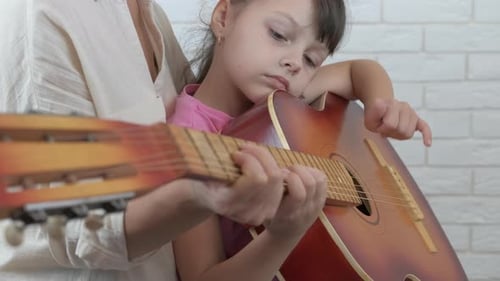 Girl learning to play guitar with adult