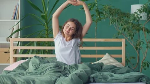 A Happy Young Woman Wakes Up in a Happy Mood Stretching Cheerfully in Bed
