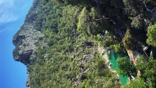 Man traveller speeding down zip line through green forest canyon.
