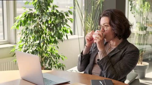 Young business woman having coffee break at work on laptop computer in office.
