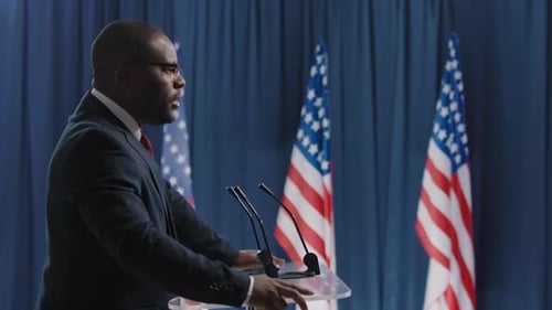 Man Giving Speech at Podium with Flags