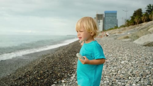 Ein kleiner Junge spielt an der Küste Er wirft Steine ins Wasser