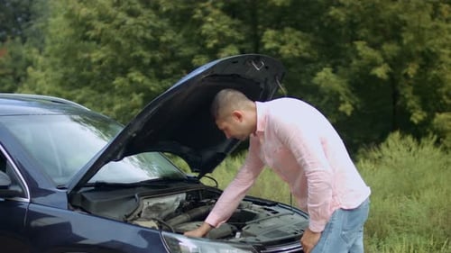 Worried Man Looking Under Hood of Car at Outdoor